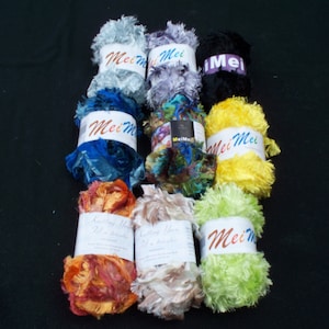 May include: Eight spools of colorful fuzzy yarn with the brand name "Mei Mei" printed on the labels. The yarn is in various colors, including blue, green, yellow, orange, and white.