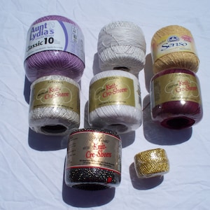 May include: Assortment of yarn spools in various colors, including purple, white, gold, and burgundy. The spools are labeled with the brand name "J&P Coats" and the yarn type "Knit-Cro-Sheen".