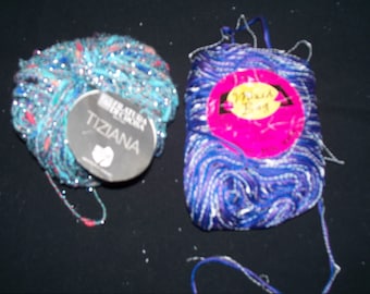 May include: Two skeins of yarn, one blue and white with silver glitter, and one teal, pink, and silver with glitter. The blue and white skein has a label that says "Magic Ball" and the teal skein has a label that says "Tiziana".