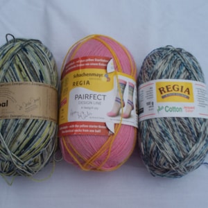 May include: Three skeins of yarn, one pink, one green and blue, and one yellow and black. The pink skein is labeled "Schachenmayr REGIA PAIRFECT DESIGN LINE" and the green and blue skein is labeled "REGIA Plus Cotton".