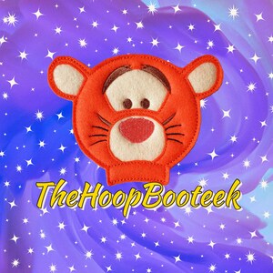 May include: Orange felt applique of a cartoon tiger with a white face, black whiskers, and red nose. The applique is on a purple background with white stars.