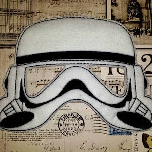 May include: A white felt mask with black stitching, depicting a Star Wars Stormtrooper helmet. The mask has a black visor and is designed to cover the eyes.
