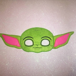 May include: Green felt mask of a cartoon character with large ears, black eyes, and a small mouth. The ears are pink.