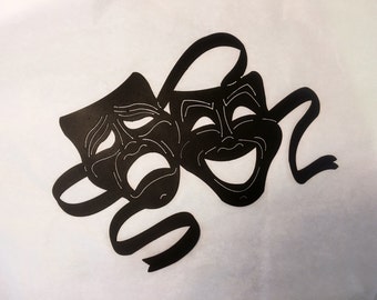 May include: Two black theatrical masks, one with a smiling expression and the other with a frowning expression, are attached to a black ribbon.