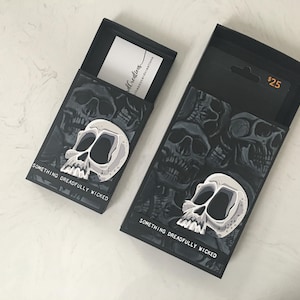 May include: Two black boxes with a skull design and the text "Something dreadfully wicked". The boxes are open and show a white card with the text "Skull Creations" and a price tag that says "$25".