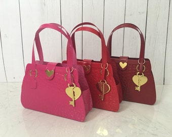 May include: Three small, decorative purses in pink, red, and burgundy. Each purse has a gold heart-shaped key charm and a gold handle.
