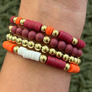 May include: A stack of bracelets with red, orange, white, and gold beads. The bracelets are made of silicone and metal.