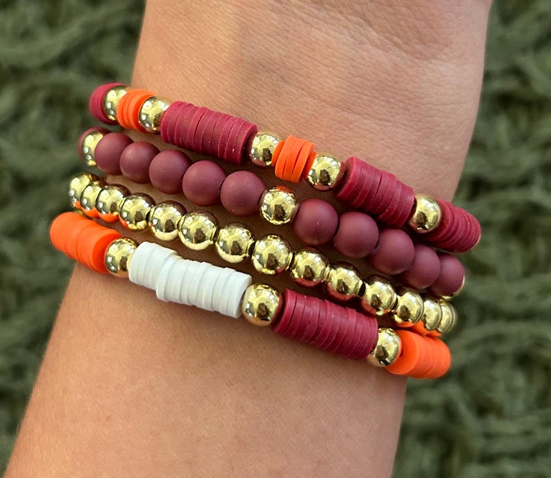 May include: A stack of bracelets with red, orange, white, and gold beads. The bracelets are made of silicone and metal.
