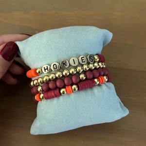 May include: A set of four bracelets with maroon and orange beads and gold beads that spell out "HOKIES".
