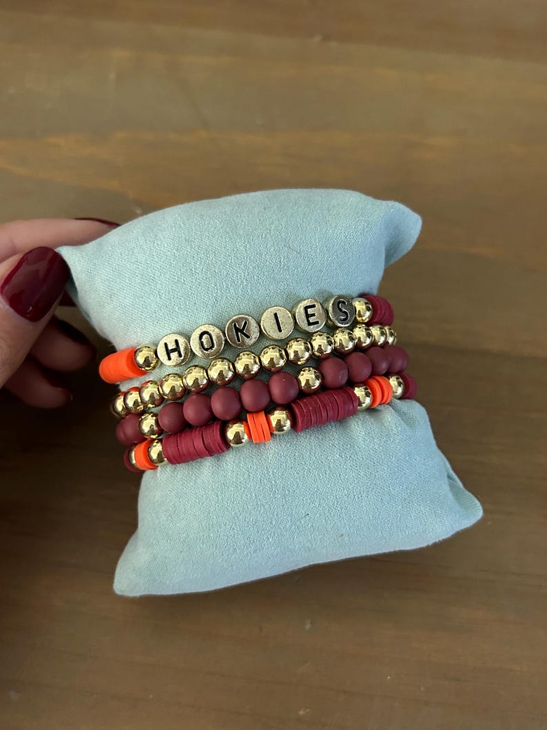 May include: A set of four bracelets with maroon and orange beads and gold beads that spell out "HOKIES".