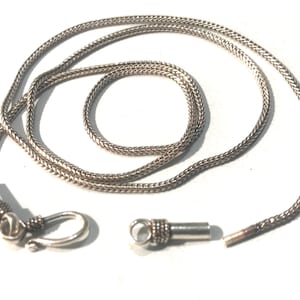 May include: A silver chain necklace with a lobster clasp and a spring ring clasp. The chain is made of small, linked silver beads.