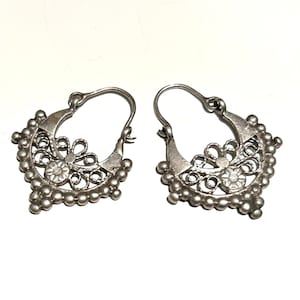 Puede incluir: Un par de pendientes de aro de plata con un delicado diseño de filigrana. Los pendientes están hechos de pequeñas cuentas redondas y tienen un motivo floral.