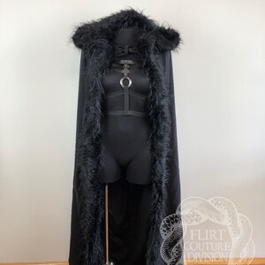 以下が含まれることがあります： 黒色のフード付きケープで、フェイクファーのトリムが付いています。ケープは長く、ゆったりとしていて、ファーは柔らかくふわふわしています。