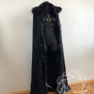 以下が含まれることがあります： フェイクファーのトリムとフードが付いたロングブラックケープ。ケープはマネキンに着用されており、ボディスにシルバーリングのディテールがあります。