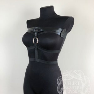 以下が含まれることがあります： リングとストラップが付いた黒い革製のハーネス。ハーネスは黒いマネキンに着せられています。