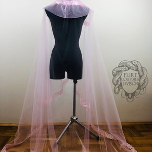 May include: A pink tulle veil with a lace trim. The veil is on a mannequin and has a large hood.