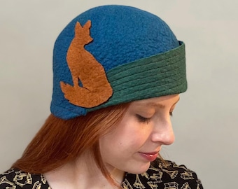 May include: A blue felt cloche hat with a green felt band and an orange felt fox silhouette.