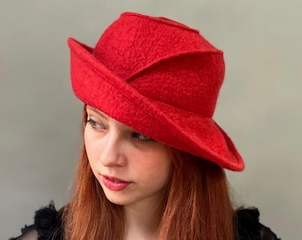 Könnte beinhalten: Ein roter Filzhut mit einem einzigartigen, gefalteten Design. Der Hut hat eine breite Krempe und eine abgerundete Krone.