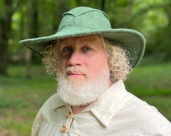 May include: A man with a white beard wearing a green felt hat with a wide brim and a white linen shirt with wooden buttons.