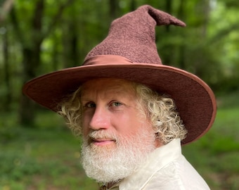 May include: A brown felt wizard hat with a wide brim and a pointed crown. The hat has a brown satin ribbon around the base of the crown.