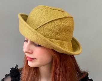 May include: A mustard yellow felt hat with a wide brim and a unique, slightly rounded crown.