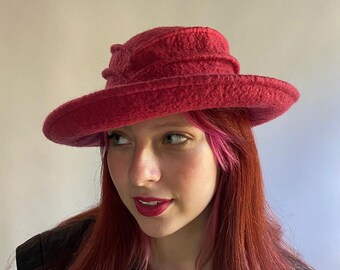 Könnte beinhalten: Ein roter Filzhut mit breiter Krempe und einem einzigartigen Design. Der Hut ist aus einem weichen, strukturierten Material gefertigt und hat eine leicht eingefallene Krone.