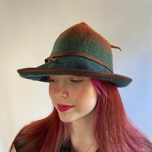 May include: A green and orange felt hat with a brown leather band and a pointed crown. The hat has a wide brim and a small, pointed tail.