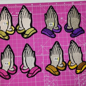 May include: Eight embroidered iron-on patches with a praying hands design. The patches are in various colors, including purple, pink, gold, and white. The patches are labeled with numbers and letters, such as 7A, 8A, 9A, and 10A.