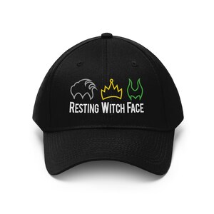 Pu&ograve; includere: Cappellino da baseball nero con la scritta bianca "RESTING WITCH FACE". Sopra il testo ci sono tre illustrazioni: una criniera di leone grigia, una corona gialla e una forma verde a forma di fiamma.