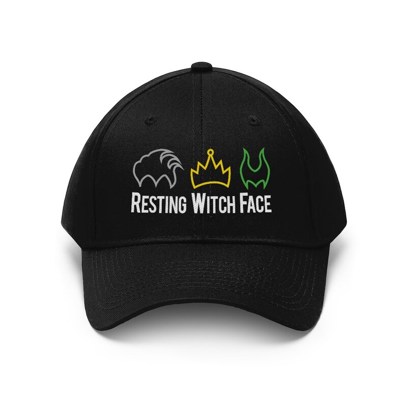 Pu&ograve; includere: Cappellino da baseball nero con la scritta bianca "RESTING WITCH FACE". Sopra il testo ci sono tre illustrazioni: una criniera di leone grigia, una corona gialla e una forma verde a forma di fiamma.