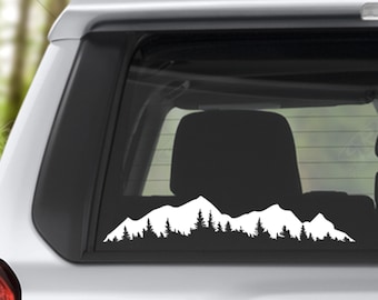 May include: White silhouette of a mountain range with trees in front of the mountains on a car window.