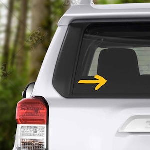 May include: A white car with a yellow arrow sticker on the rear window.