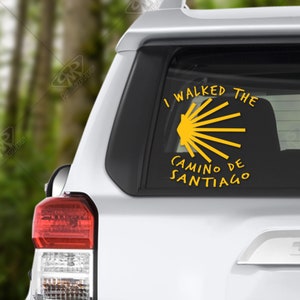 May include: A yellow sticker on the back of a white car that says "I walked the Camino de Santiago" with a yellow scallop shell symbol.