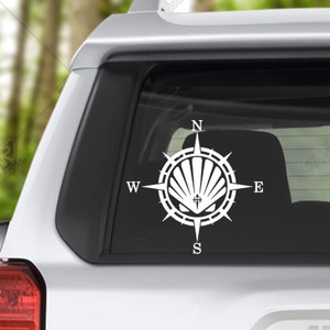 May include: White vinyl decal of a compass with a scallop shell in the center. The compass points are labeled N, S, E, and W.