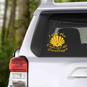 May include: A yellow vinyl sticker with the text "I did the Camino de Santiago" and a scallop shell with a cross on it.