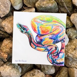 Op de afbeelding: Kleurrijke slangenillustratie op wit papier. Het kunstwerk toont een regenboogkleurige slang met levendige tinten blauw, groen, geel en rood. De tekst "ART BY EILEE" staat linksonder.