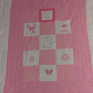 May include: A pink and white quilt with a patchwork design. Each square features a different embroidered design, including butterflies, hearts, and the words "Forever & Always" and "Strength & Hope".