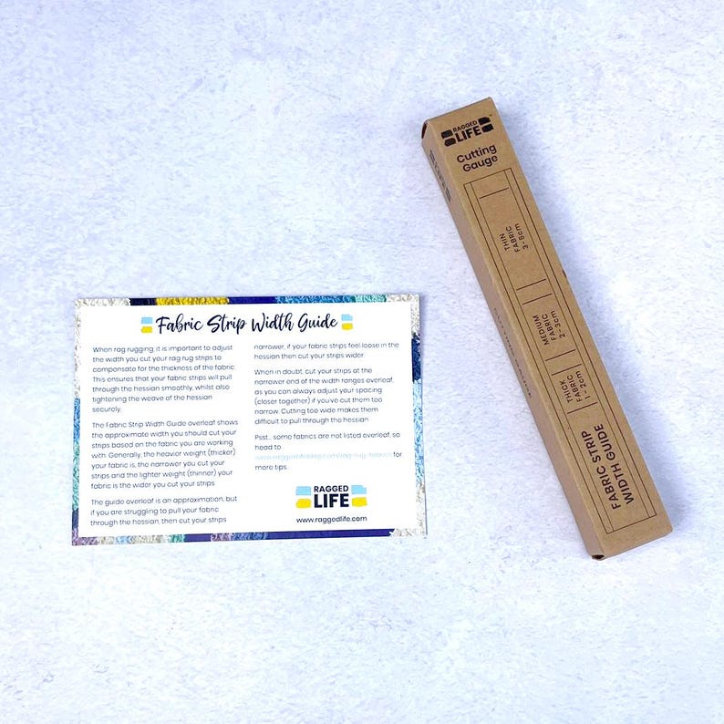 Hand using rag rug cutting gauge to cut fabric strips evenly, time-saving tool for rug hooking and peg loom weaving. Shown in cardboard packaging with fabric strip width guide