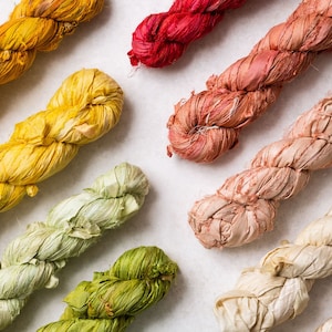 May include: Assortment of colourful silk ribbon, twisted and knotted, in shades of yellow, green, pink, red, and white.
