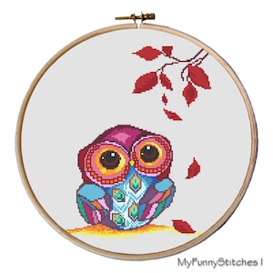May include: A cross-stitch embroidery project in a round wooden hoop featuring a stylized owl with vibrant pink, blue, and purple plumage. The owl sits on a yellow ground with red leaves falling from a branch above. Text reads MyFunnyStitches.