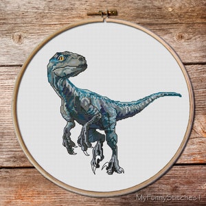 May include: A cross-stitch embroidery piece featuring a blue raptor dinosaur with yellow eyes, displayed in a round wooden hoop. The design is stitched on white fabric, and the text MyFunnyStitches is visible in the bottom right corner.