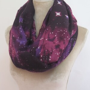 May include: A purple and black infinity scarf with a white galaxy print. The scarf is made of a soft, lightweight fabric and is perfect for adding a touch of style to any outfit.