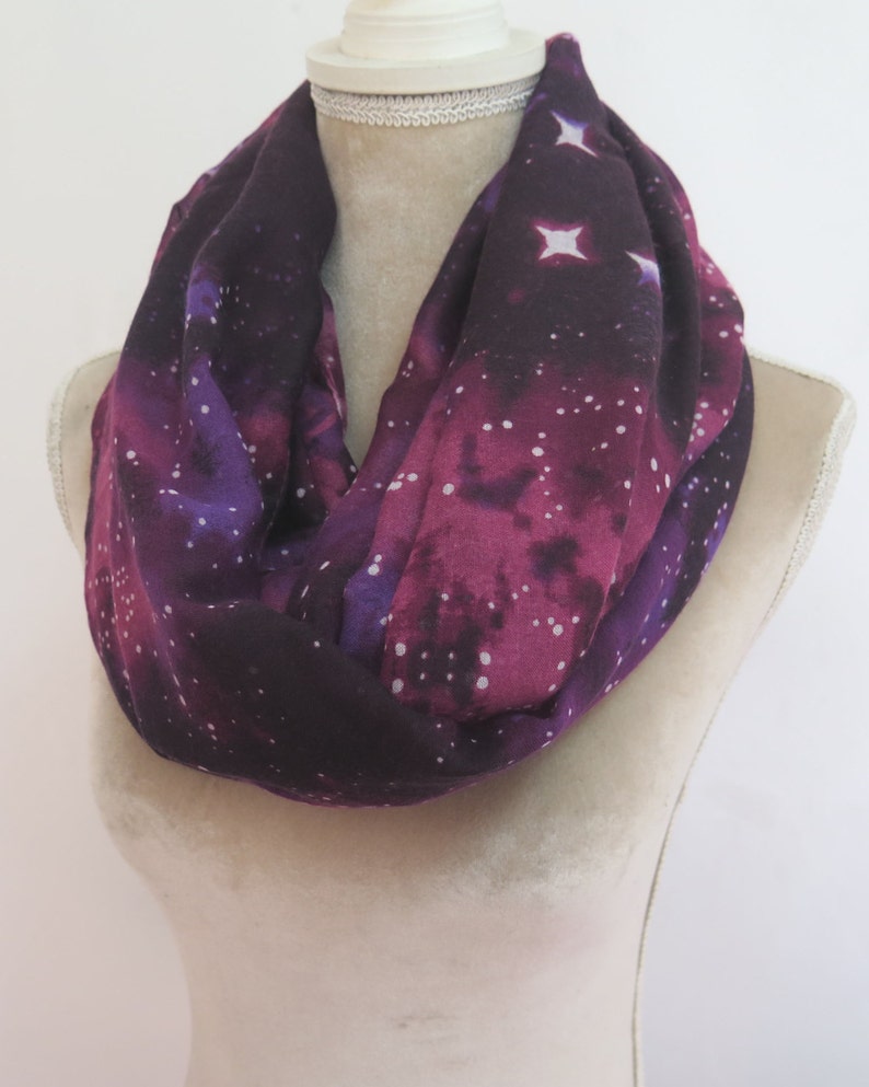 May include: A purple and black infinity scarf with a white galaxy print. The scarf is made of a soft, lightweight fabric and is perfect for adding a touch of style to any outfit.