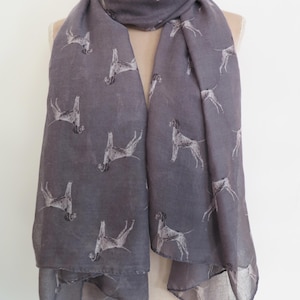 May include: A gray scarf with a repeating pattern of white dog illustrations. The scarf is draped over a mannequin, showcasing its length and design. The fabric appears lightweight and suitable for cooler weather.