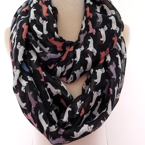 May include: Black infinity scarf with a white dachshund print. The dachshunds are in various shades of pink, blue, and orange.