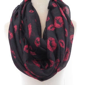 May include: Black infinity scarf with a repeating pattern of red lips. The scarf is displayed on a white mannequin and is made of a lightweight fabric. The lips are in a bold, lipstick-like style.