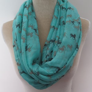 May include: A turquoise infinity scarf with a repeating pattern of black horses. The scarf is made of a soft, lightweight fabric.