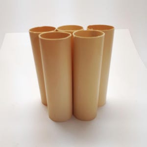 May include: Five cylindrical objects in a light tan colour are arranged together. The objects are open at the top and appear to be made of a smooth material. The cylinders are standing upright against a white background.