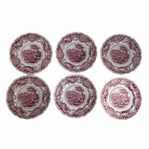 Puede incluir: Juego de seis platos de cena de porcelana rosa y blanca con borde festoneado y diseño floral. Cada plato presenta una imagen central de una escena de paisaje.