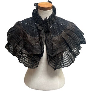 May include: A black lace shawl with a ruffled collar and beaded embellishments. The shawl is on a white mannequin.